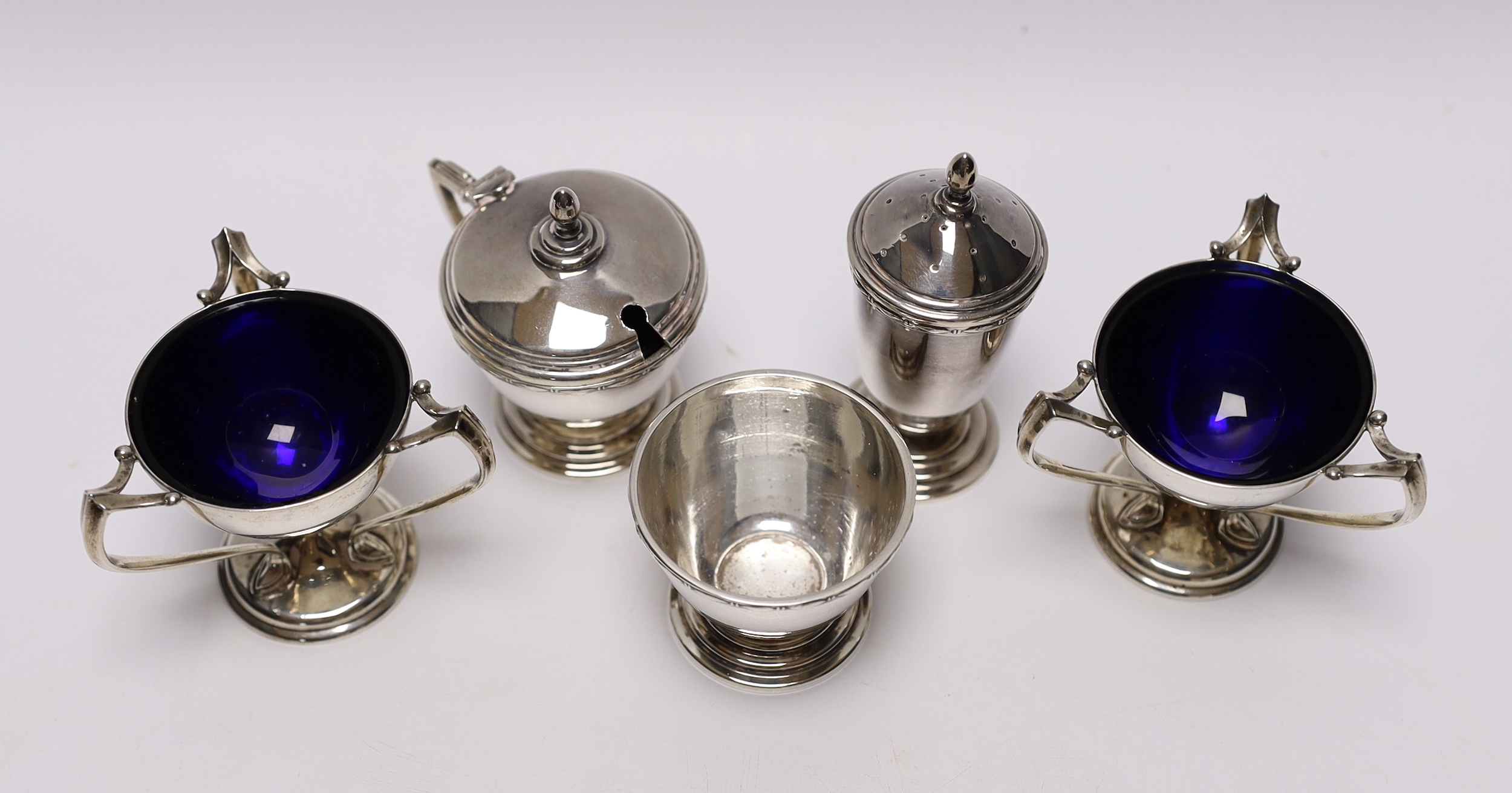 A pair of Edwardian Art Nouveau silver tri-handled salts, Richard Richardson, Sheffield, 1905, height 59mm, together with a later silver three piece condiment set, with two spoons (one plated).